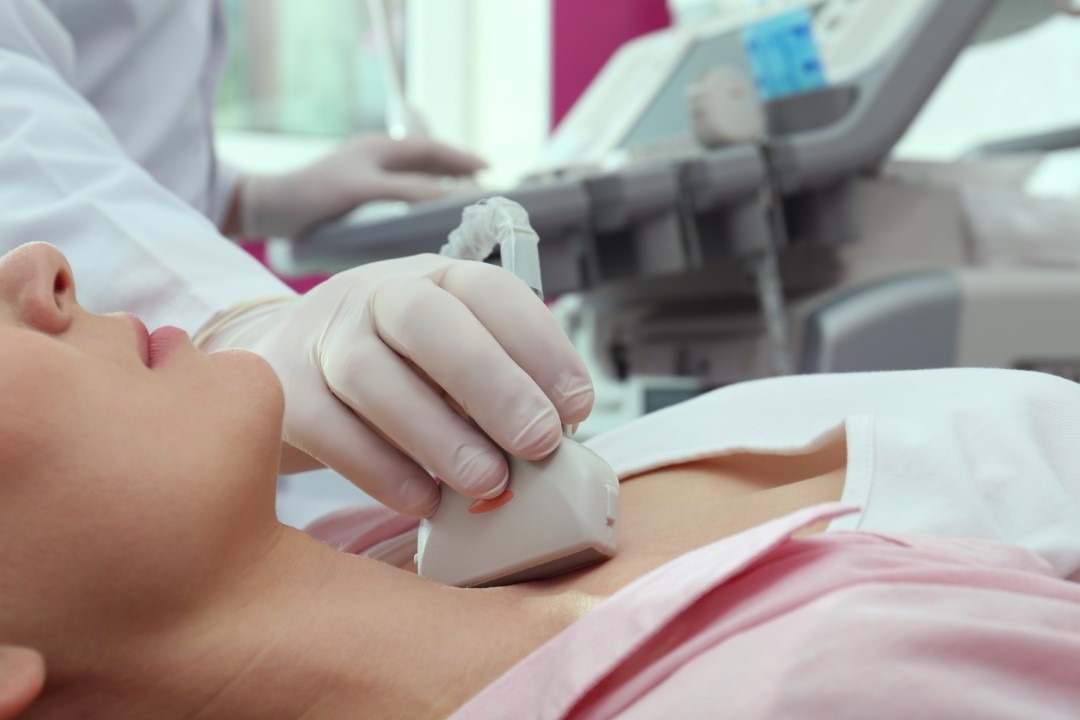 Doctor conducting ultrasound examination of thyroid gland in cli